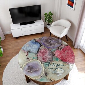 May include: A round coffee table with a decorative agate stone top. The table has a wooden base and a top with blue, purple, and red agate stones. The text "Artisan enterprise" is printed on the top.