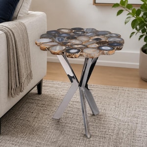 May include: A decorative side table with a unique agate stone top. The table features a mosaic of polished agate slices in shades of gray, blue, and brown. The table has a polished chrome base with three legs. The table is a stylish accent piece.