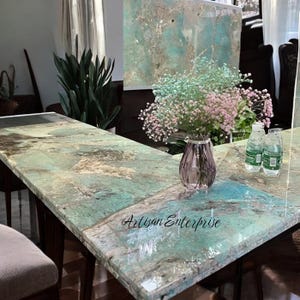Könnte beinhalten: Ein rechteckiger Tisch mit einer türkis-braun marmorierten Oberfläche. Eine Vase mit rosa und grünen Blumen steht auf dem Tisch. Der Text "Artisan Enterprise" ist auf der Tischoberfläche zu sehen.