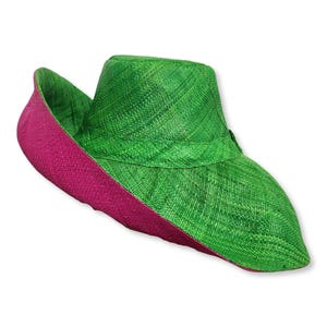 May include: A wide-brimmed hat crafted from woven material, featuring a vibrant green crown and upper brim, contrasted by a deep magenta underside on the brim. The hat has a structured shape with a distinct band separating the crown from the brim.