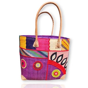 May include: A colorful patchwork tote bag with leather handles. The bag features a vibrant mix of purple, pink, yellow, and blue woven panels, with decorative embroidered circles and leaf-like shapes. The handles are a light brown color.