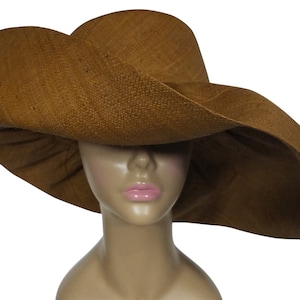 May include: A wide-brimmed sun hat in a warm brown hue. The hat features a large, gently curved brim and a woven texture, offering ample shade. The hat is displayed on a mannequin head.