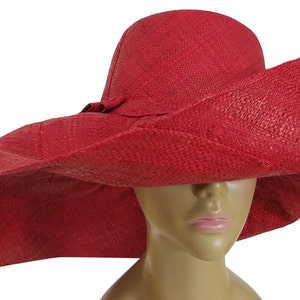 May include: A vibrant red sun hat with a wide brim and a slightly curved crown. The hat is made of woven material and features a small bow detail. The hat is designed to provide shade and protection from the sun.