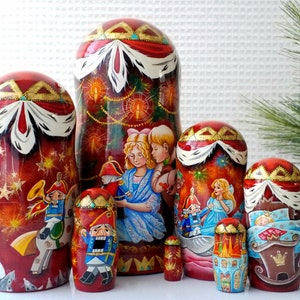 May include: A set of six red and gold Russian nesting dolls, or matryoshka dolls, depicting a Christmas scene with a nutcracker, a girl, and a boy. The dolls are painted with intricate details and are a festive addition to any holiday decor.