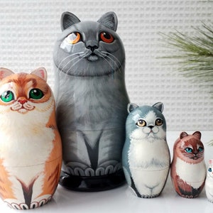 May include: A set of five hand-painted wooden nesting dolls, each depicting a different cat. The dolls range in size, with the largest being gray and the smallest white. The cats have various colors, including orange, gray, and brown.