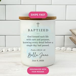 May include: A white candle with a wooden lid, featuring the word "BAPTIZED" and a cross. The candle includes a personalized message and a Bible verse. The design has a watercolor effect with blue and green hues.