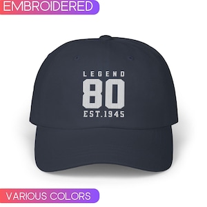 May include: Navy blue baseball cap with white embroidered text that reads "LEGEND 80 EST.1945". The cap has a curved brim and a classic six-panel design. The text is centered on the front of the cap.