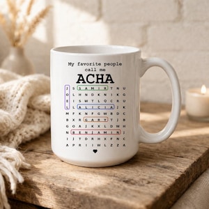 May include: White ceramic mug with the text "My favorite people call me ACHA" and a word search grid with names like Samir, Alicia, Gary, and Benjamin. The mug sits on a wooden surface.