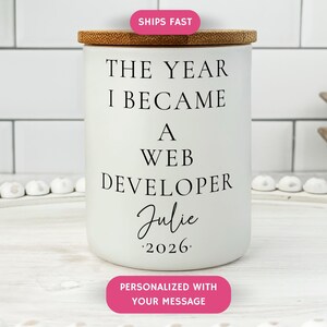 May include: A white ceramic jar with a bamboo lid. The jar has the text "THE YEAR I BECAME A WEB DEVELOPER Julie 2026" in black. The jar is personalized with a message.