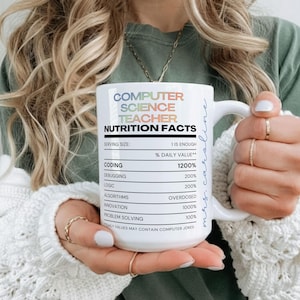 May include: White ceramic mug with the text "COMPUTER SCIENCE TEACHER NUTRITION FACTS". The mug features a nutrition facts label with humorous entries like "Coding 1200%" and "Debugging 200%", and is held by a person.