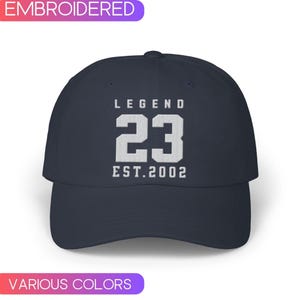 Puede incluir: Una gorra de béisbol azul marino con texto blanco bordado que dice "LEGEND 23 EST. 2002".