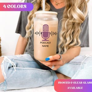 May include: A clear glass tumbler with a bamboo lid and a straw. The tumbler features a purple microphone graphic with sound wave lines and the text "PODCAST NAME". The top left corner has the text "4 COLORS". The bottom right corner has the text "FROSTED & CLEAR GLASS AVAILABLE".