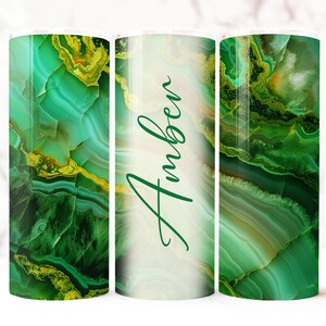 May include: A tumbler with a green and gold agate design. The word "Amber" is written in a cursive font on the tumbler. The tumbler has a white background and a stainless steel interior.