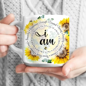 Może przedstawiać: Biały kubek ceramiczny z motywem słonecznika i napisem "Jestem" w środku. Kubek jest otoczony kołem słów i wersetów biblijnych, w tym "Wybrany", "Nigdy sam", "Zawsze kochany", "Zdolny", "Niesamowity", "Silny", "Stworzony", "Wystarczający", "Zwycięski" i "Piękny".