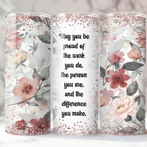 Pode incluir: Um copo com tema floral com fundo branco e um design de flores rosa, vermelhas e cinzentas. O copo tem o texto: "May you be proud of the work you do, the person you are, and the difference you make."