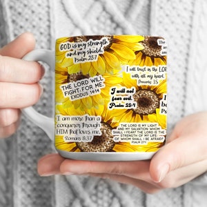 May include: White ceramic mug with a sunflower design and inspirational quotes from the Bible. The quotes include "God is my strength and my shield", "The Lord will fight for me", "I will not fear evil", "I am more than a conqueror through Him that loves me", "I will trust in the Lord with all my heart", and "The Lord is my light and my salvation".