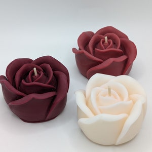 May include: Three rose-shaped candles, one white and two burgundy.