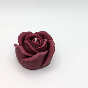 May include: A single burgundy rose-shaped candle with a white wick.