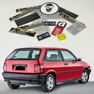 May include: A red Fiat Tipo 2010 hatchback with a black bumper and black trim around the windows. The car has a sticker on the back window that says "Tipo 2010". There are several warning stickers on the white background.