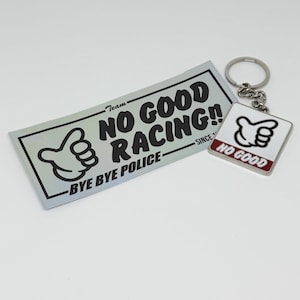 以下が含まれることがあります： 親指を立てた黒いグラフィックと「Team NO GOOD RACING!! BYE BYE POLICE」の文字が描かれた長方形の銀色のステッカーと、白い背景に黒い親指のグラフィックと赤い「NO GOOD」の文字が描かれた正方形の金属製キーホルダー。