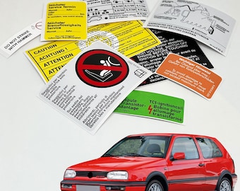 Puede incluir: Un Volkswagen Golf rojo con varias pegatinas y etiquetas de advertencia. Las pegatinas están en varios idiomas, incluidos inglés, alemán, francés e italiano. Las pegatinas advierten sobre precauciones de seguridad, como evitar golpear el coche con un martillo, y proporcionan instrucciones para el mantenimiento y la reparación.