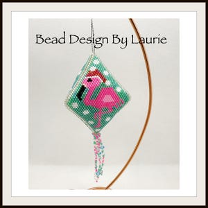 May include: A pink flamingo wearing a Santa hat is beaded on a green and white square ornament with a beaded fringe. The ornament is hanging from a gold stand. "Bead Design By Laurie" is written above the ornament.