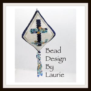 Puede incluir: Un adorno de cruz de cuentas blancas, azules y doradas con forma de diamante y flecos de cuentas. El adorno está colgado de una cuerda blanca. El texto "Bead Design By Laurie" está escrito debajo del adorno.