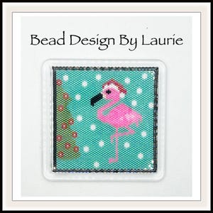 May include: A pink flamingo wearing a Santa hat is beaded on a turquoise background with white polka dots. The flamingo is standing next to a beaded green Christmas tree with red ornaments.