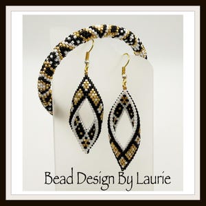 Puede incluir: Un conjunto de joyas de cuentas con una pulsera y un par de pendientes. La pulsera y los pendientes tienen un patrón negro, blanco y dorado. Los pendientes tienen forma de lágrima con un recorte en forma de diamante. El texto "Bead Design By Laurie" está en la parte inferior.