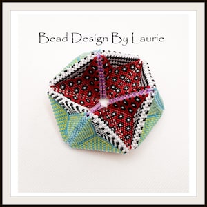Puede incluir: Una forma geom&eacute;trica de cuentas multicolores con una abertura en forma de estrella en el centro. La forma est&aacute; hecha de cuentas rojas, blancas, negras, verdes y azules. El texto "Bead Design By Laurie" es visible en la parte superior de la imagen.