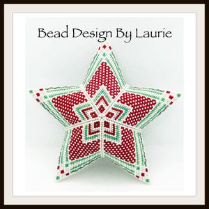 Può includere: Un ornamento a forma di stella in perline rosse e verdi su sfondo bianco. La stella è realizzata con piccole perline e presenta un motivo geometrico. Il testo "Bead Design By Laurie" è stampato nella parte superiore dell'immagine.