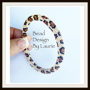 Könnte beinhalten: Ein Perlenarmband mit einem beigen, schwarzen und braunen Leopardenmuster. Der Text "Bead Design By Laurie" ist auf dem Bild zu sehen. Das Armband wird von einer Hand gehalten.