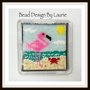 May include: A beaded square featuring a pink flamingo on a beach with a red crab, turquoise water, and a yellow sun. The text "Bead Design By Laurie" is at the top. The artwork is encased in a clear, square frame.