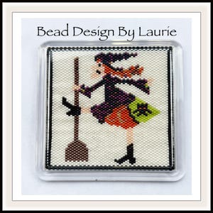 May include: A beaded design of a witch with a broom, wearing a purple and orange dress, a black hat, and a green bag. The design is framed in a clear plastic frame with a black border. The text "Bead Design By Laurie" is at the top of the frame.
