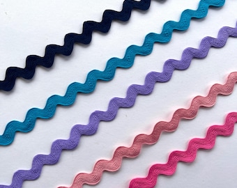 May include: Five parallel strips of rickrack trim arranged diagonally. The colors include dark navy blue, bright turquoise, light purple, soft peach, and vibrant hot pink. Each strip features a consistent wavy, zigzag pattern throughout its length.