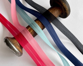 May include: Five spools of ribbon in various colors, including pink, blue, and black, are wound around a wooden spool. The ribbons are sheer and have a subtle sheen.