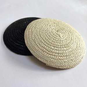 May include: Two round woven placemats. One is black, and the other is a natural beige colour. The placemats are made of a tightly woven material, with a spiral pattern radiating from the centre. They are suitable for dining and home decor.