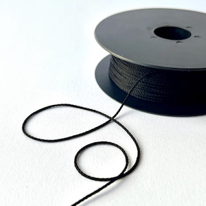 May include: A black spool of thread with a length of thread unwound and looped on a white surface. The thread is a dark, solid colour. The spool is black and round.