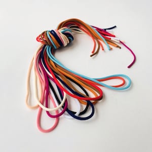 Può includere: Un insieme di cordini elastici colorati, tra cui rosso, arancione, giallo, verde, blu, viola, rosa e bianco. I cordini sono disposti in un nodo sciolto, con le estremità dei cordini che pendono.