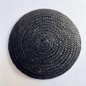 May include: A round, black woven hat with a spiral pattern. The hat is made of a tightly woven material, and the color is a deep, solid black. The hat is a simple, classic design.