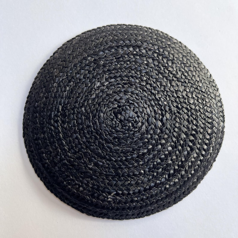 May include: A round, black woven hat with a spiral pattern. The hat is made of a tightly woven material, and the color is a deep, solid black. The hat is a simple, classic design.