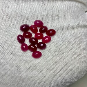 Puede incluir: Una colección de piedras preciosas ovaladas en varios tonos de rosa y rojo, expuestas sobre una superficie de tela blanca.