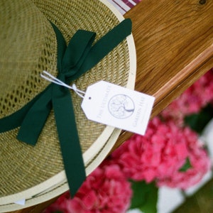 May include: A straw hat with a green ribbon and a white tag that says "The Farmhouse Garden Hat".