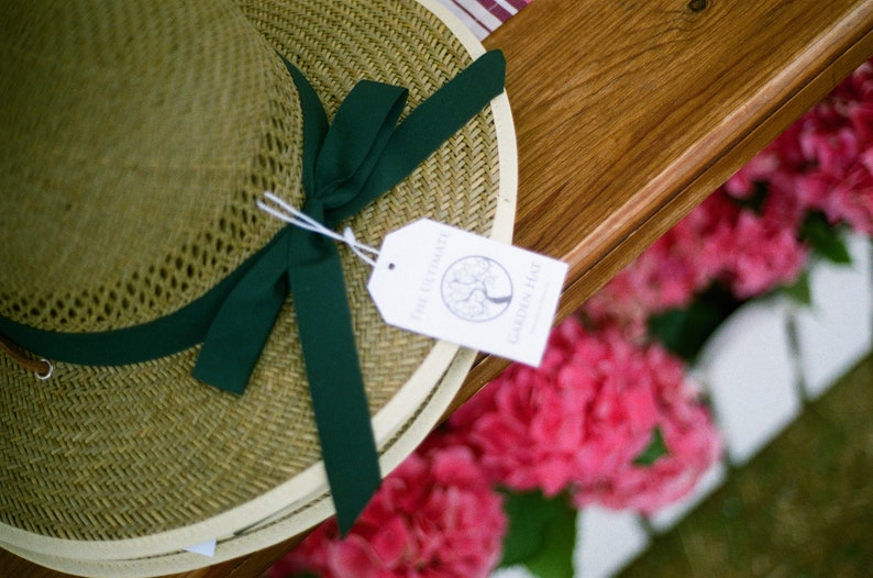May include: A straw hat with a green ribbon and a white tag that says "The Farmhouse Garden Hat".