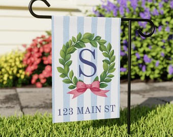 Könnte beinhalten: Eine Gartenflagge mit blau-weiß gestreiftem Hintergrund. Sie zeigt einen grünen Kranz mit dem marineblauen Buchstaben "S", eine rosa Schleife und den Text "123 MAIN ST". Die Flagge ist an einem schwarzen Metallständer befestigt.