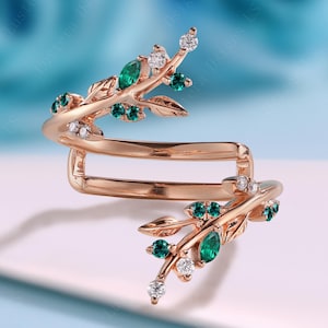 Può includere: Un anello in oro rosa dal design unico. L'anello presenta un motivo a forma di ramo ornato da pietre preziose verde smeraldo e trasparenti. Il design dell'anello si avvolge attorno al dito, creando un look distintivo ed elegante.