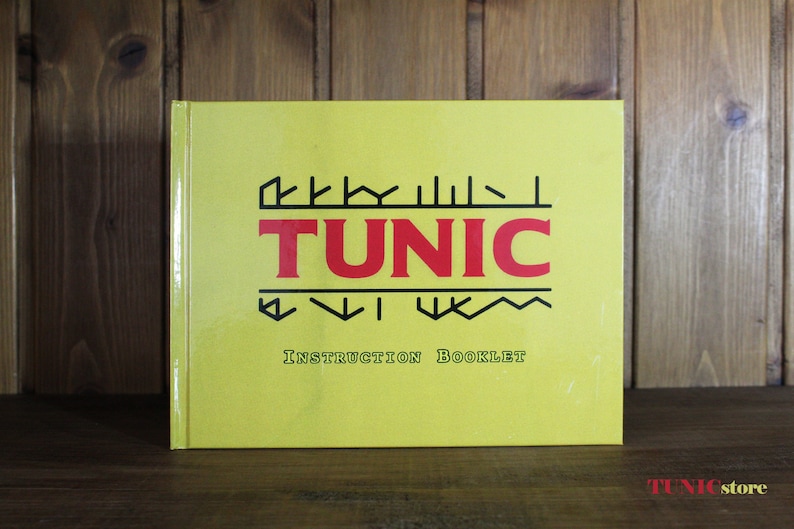 Puede incluir: Un folleto de instrucciones amarillo para el videojuego "TUNIC". El folleto tiene texto negro y rojo y un logotipo estilizado con el t&iacute;tulo del juego.