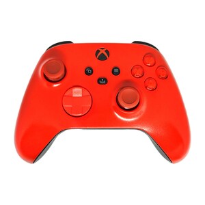 Puede incluir: Un mando Xbox rojo brillante con detalles en negro. El mando presenta el logotipo de Xbox, un mando en cruz, dos palancas analógicas y varios botones. El diseño es simétrico y ergonómico, con un acabado brillante.
