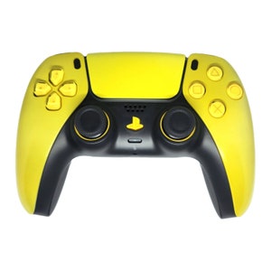 May include: A yellow and black game controller with a PlayStation logo. The controller has a yellow top and buttons, with black grips and joysticks. The directional pad and action buttons are yellow.