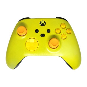Könnte beinhalten: Ein limettengrüner Xbox-Controller mit orangefarbenen und gelben Akzenten. Der Controller hat ein schwarzes Xbox-Logo, orangefarbene Thumbsticks und gelbe Aktionstasten. Er verfügt über schwarze Griffe und ein Steuerkreuz.